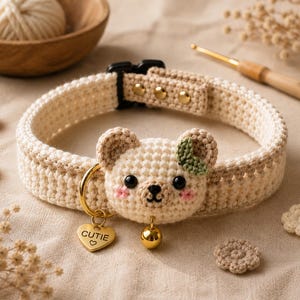 Peut inclure: Un collier pour animal en crochet couleur crème avec une tête d'ours centrale dotée d'yeux noirs, d'un nez brodé et de joues roses. Le collier comprend un anneau en métal doré, une breloque en forme de cœur gravée CUTIE et une clochette dorée.