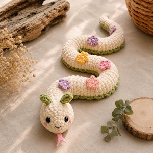Peut inclure: Un serpent en crochet de couleur crème avec un dessous vert et deux petites feuilles vertes sur la tête. Le corps est décoré de petites fleurs en crochet multicolores dans des tons de violet, jaune et rose. Il a des yeux noirs et une langue rose.