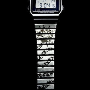 May include: A black and silver Casio digital watch with a chain-link and sunburst design on the band. The watch face displays the time as 9:04:16 PM. The watch has the text "CASIO" and "ALARM CHRONOGRAPH".