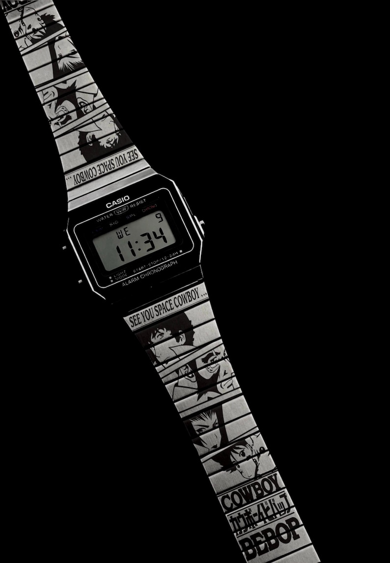May include: Black Casio digital watch with a silver band featuring anime character illustrations and the text "SEE YOU SPACE COWBOY...". The watch face displays the time as 11:34.