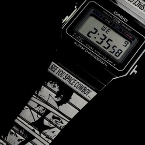 May include: Black Casio digital watch with a silver band featuring anime character illustrations. The watch face displays the time 2:35:58. The band reads "SEE YOU SPACE COWBOY..."