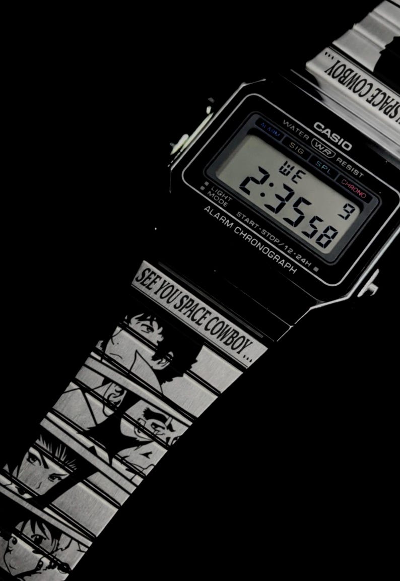 May include: Black Casio digital watch with a silver band featuring anime character illustrations. The watch face displays the time 2:35:58. The band reads "SEE YOU SPACE COWBOY..."
