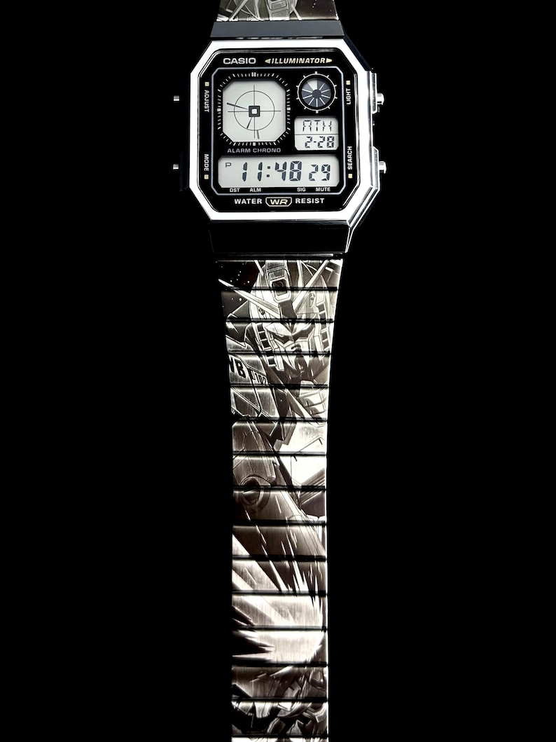 May include: A digital Casio watch with a black and silver design. The watch face displays the time and date. The watch band features a detailed graphic pattern. The watch has the text "CASIO ILLUMINATOR" and "WATER WR RESIST".