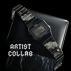 May include: A black digital Casio watch with a metal band featuring etched flame and spiral patterns. The watch face displays the time 7:24:13 and the date 16. The text ARTIST COLLAB is printed in a bold, gothic-style font on the left side.