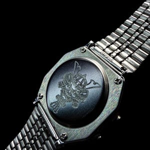 May include: A silver-toned wristwatch featuring a metallic link band and a circular case back. The center of the case back displays a detailed laser-engraved illustration of a traditional samurai helmet, known as a kabuto, centered on a dark surface.