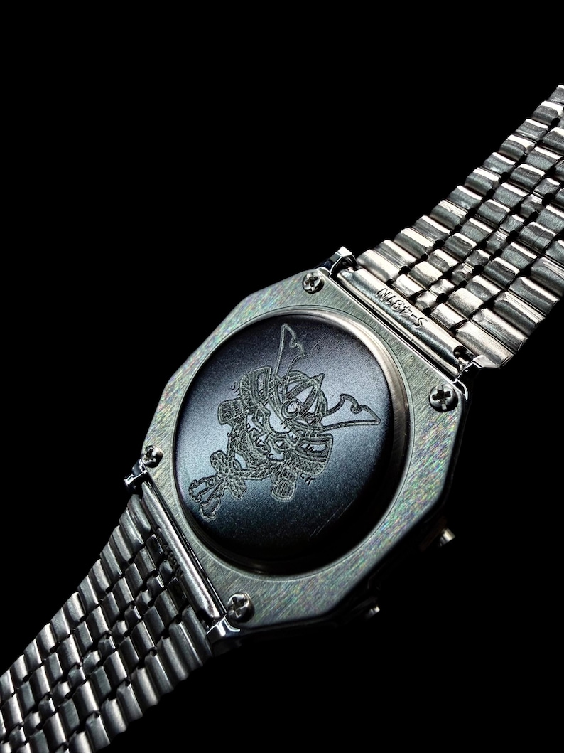 May include: A silver-toned wristwatch featuring a metallic link band and a circular case back. The center of the case back displays a detailed laser-engraved illustration of a traditional samurai helmet, known as a kabuto, centered on a dark surface.
