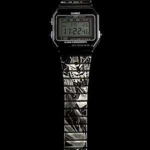 May include: A black Casio digital watch with a silver patterned band. The watch face displays the time, day, and date. The watch has the text "CASIO" and "WATER RESIST" printed on the face.