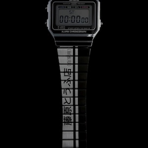 May include: A Casio digital watch with a black and silver strap. The watch face shows "00:00:00" and the Casio logo. The strap has Japanese text. The watch is set against a black background.