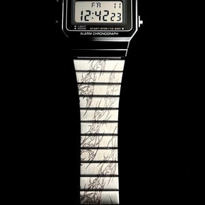 May include: Black Casio digital watch with a silver band featuring a tribal design. The watch face displays the time, day, and date. The watch has the text "CASIO" and "ALARM CHRONOGRAPH".