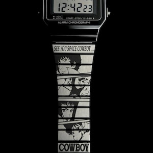 May include: Black Casio digital watch with a silver band featuring anime character illustrations and the text "SEE YOU SPACE COWBOY..." and "COWBOY カウボーイビバップ BEBOP". The watch displays the time 12:42:23.