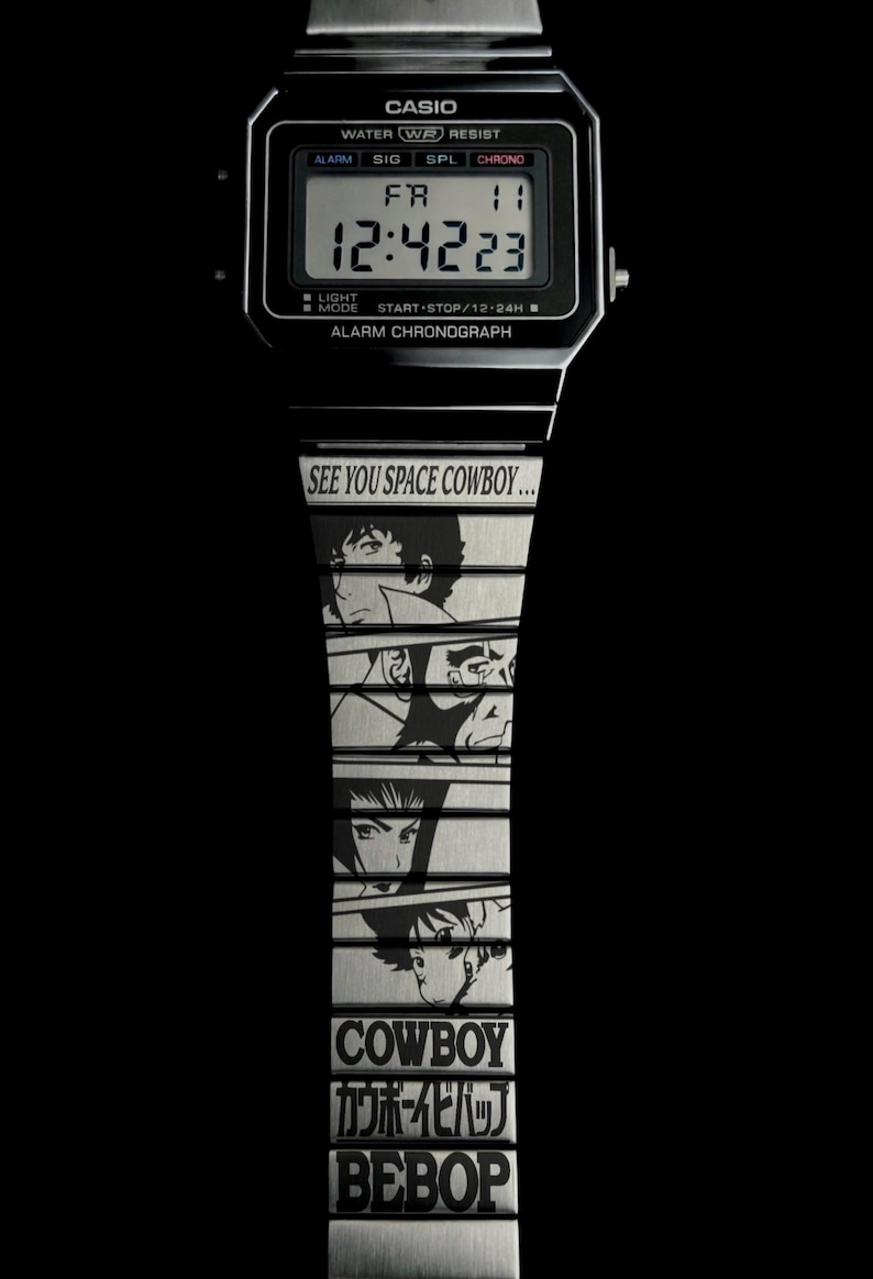 May include: Black Casio digital watch with a silver band featuring anime character illustrations and the text "SEE YOU SPACE COWBOY..." and "COWBOY カウボーイビバップ BEBOP". The watch displays the time 12:42:23.