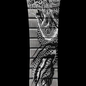 Puede incluir: Una correa de reloj de metal plateado cepillado con un dise&ntilde;o de drag&oacute;n grabado en blanco y negro que se extiende por los eslabones individuales. La intrincada ilustraci&oacute;n muestra un drag&oacute;n largo y serpentino con escamas y garras.