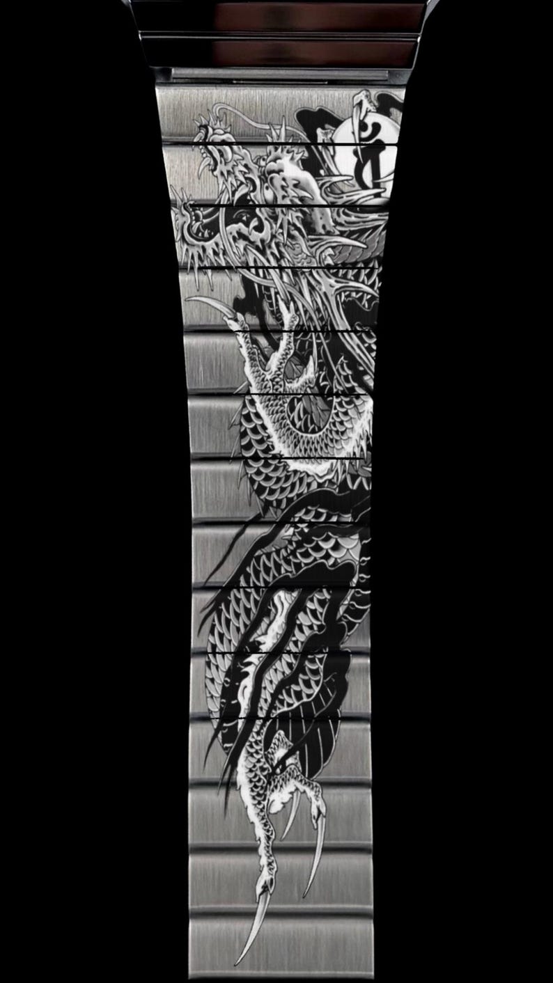 Puede incluir: Una correa de reloj de metal plateado cepillado con un dise&ntilde;o de drag&oacute;n grabado en blanco y negro que se extiende por los eslabones individuales. La intrincada ilustraci&oacute;n muestra un drag&oacute;n largo y serpentino con escamas y garras.