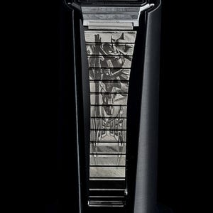 May include: A black digital watch with a silver band featuring a Batman design. The watch is displayed on a black stand against a black background. The watch face displays the Casio brand.