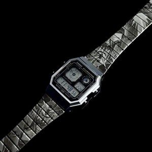 May include: A silver Casio digital watch with a patterned band. The watch face displays the time, date, and other functions. The band has a repeating geometric design. The watch is set against a black background.