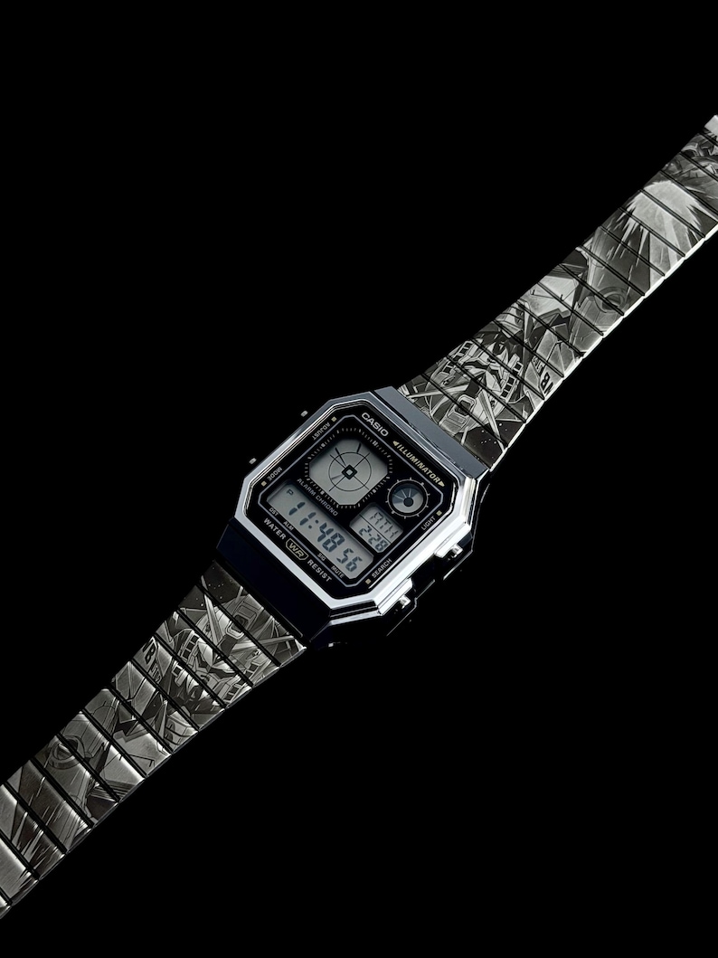 May include: A silver Casio digital watch with a patterned band. The watch face displays the time, date, and other functions. The band has a repeating geometric design. The watch is set against a black background.