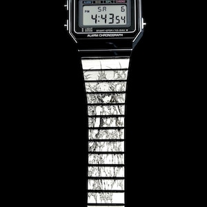 May include: Black Casio digital watch with a custom band featuring a black and white anime illustration. The watch face displays the time as 4:43:54 PM. The band has a repeating pattern of a manga-style character.