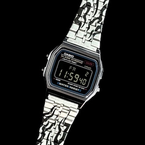 May include: A silver-tone digital wristwatch with a black face and a metal link band featuring a black flame pattern. The watch display shows the text CASIO, ALARM CHRONO, WR, Lithium, WATER RESIST, and the time 11:59:40 with the day FR 2.