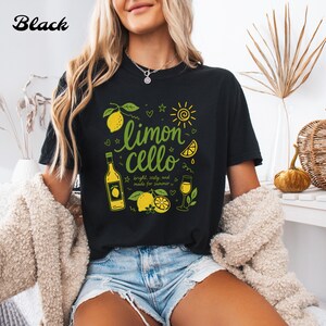 May include: A black t-shirt featuring a graphic print with the text "limoncello" in green, accompanied by illustrations of lemons, a bottle, a glass, and a sun. The design includes the text "bright, zesty, and made for summer" in small font.