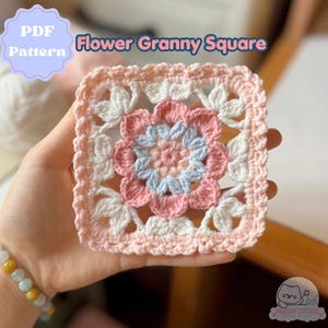 Può includere: Un quadrato granny all'uncinetto con un motivo floreale. Il fiore centrale è rosa e azzurro, circondato da petali bianchi e rosa. Il testo "PDF Pattern" e "Flower Granny Square" sono visibili.