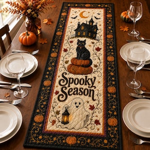 May include: A rectangular quilted table runner featuring a cream-colored center panel with the text Spooky Season, a black cat on pumpkins, a haunted house, and a ghost holding a lantern, all surrounded by a black border with orange pumpkin motifs.