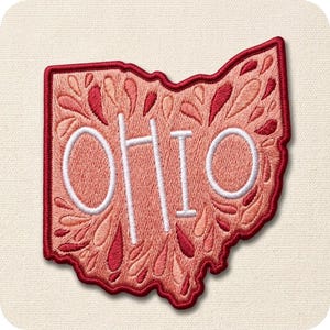 May include: Embroidered patch in the shape of Ohio, featuring the state name in white. The patch has a red border and is filled with a floral design in shades of pink and red. The patch is on a cream-colored background.