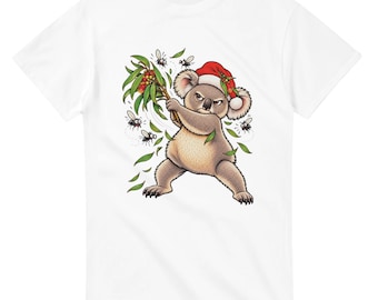 May include: A white short-sleeved t-shirt featuring a graphic illustration of a grumpy koala wearing a red and white Santa hat. The koala is holding a branch of eucalyptus with berries and swatting at several small flies buzzing around it.