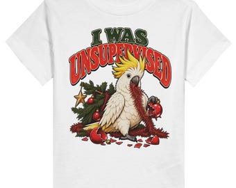May include: A white short-sleeved t-shirt featuring a graphic of a white cockatoo with a yellow crest. The bird is holding red tinsel and a broken red ornament. The text I WAS UNSUPERVISED is printed in red and green above the bird.