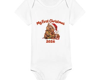 May include: A white short-sleeved baby bodysuit featuring a graphic of a brown wombat wearing a red Santa hat, wrapped in colourful Christmas lights next to a gift box. The text reads My First Christmas 2026 in red lettering.