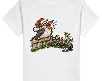 May include: A white short-sleeve t-shirt featuring a graphic of a kookaburra wearing a red Santa hat. The bird sits on a wooden fence draped with colourful Christmas lights, next to a fallen wire reindeer frame tangled in the light string.