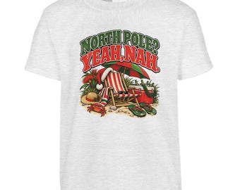 May include: A light grey t-shirt featuring a graphic of a beach scene with a striped deck chair, a red and green umbrella, a Santa hat, a crab, a straw hat, and a cooler. The text reads NORTH POLE? YEAH, NAH. in green and red letters.