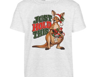 May include: A light grey t-shirt featuring a graphic of a kangaroo wearing a Santa hat. The kangaroo has a pouch filled with Christmas gifts and a small koala. The text "JUST HOLD THIS" is printed in large green and red letters next to it.
