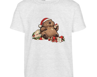 May include: A light grey short-sleeve t-shirt featuring a graphic of a brown wombat wearing a red Santa hat. The wombat is eating food with crumbs on its face, surrounded by scattered treats and a small card that reads Merry Christmas Anyway.