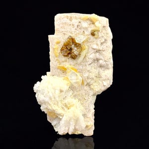 Puede incluir: Espécimen mineral natural con una matriz beige claro, que presenta grupos de formaciones cristalinas blancas. Varias estructuras cristalinas de color marrón dorado están incrustadas, creando un contraste con el fondo más claro.