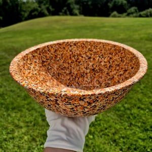 May include: A round bowl featuring a speckled pattern in shades of orange, yellow, black, and white. The bowl has a smooth, curved interior and a wide, circular rim, showcasing a dense, multi-colored confetti-like texture across its entire surface.