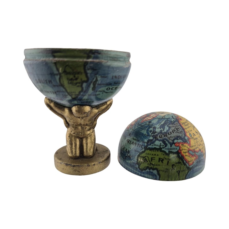 Op de afbeelding: Een miniatuur wereldbolsculptuur. De bovenste helft van de wereldbol wordt ondersteund door een goudkleurige Atlasfiguur. De wereldbol is blauw en groen, met continenten en oceanen beschreven. Een aparte wereldbolhelft ligt ernaast.