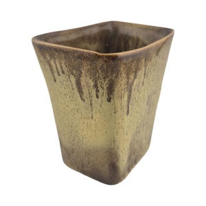Może przedstawiać: Kwadratowy kubek ceramiczny z reaktywnym szkliwem w jasnobrązowym kolorze z ciemnobrązowymi wzorami zacieków spływającymi od krawędzi. Naczynie ma lekko zwężającą się sylwetkę z zaokrąglonymi rogami oraz gładkie, błyszczące wykończenie powierzchni.