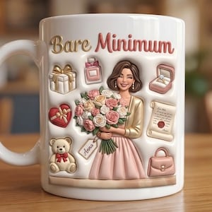 Puede incluir: Taza de cerámica blanca con las palabras "Bare Minimum" en letras doradas y rojas. La taza presenta un diseño 3D de una mujer sosteniendo flores, rodeada de cajas de regalo, un frasco de perfume, una caja de anillos, un corazón, un oso de peluche, un bolso y un pergamino.