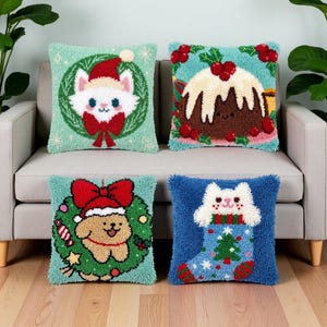 May include: Four square punch needle throw pillows featuring holiday designs. One shows a white cat in a wreath, another a Christmas pudding, a third a puppy in a wreath with a red bow, and the fourth a white cat inside a blue Christmas stocking.