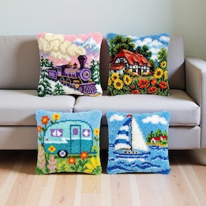May include: Four decorative throw pillows with colorful, textured designs. One features a purple train, another a cottage with sunflowers, a third a blue camper, and the last a sailboat on the water. The pillows are on a gray sofa.