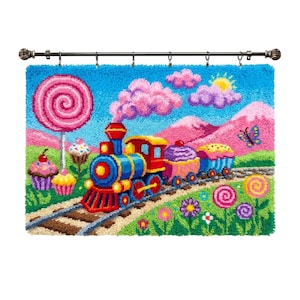Puede incluir: Un tapiz rectangular de ganchillo que muestra un tren de vapor colorido viajando por un paisaje con montañas rosas, cielo azul, nubes rosas, un sol amarillo, cupcakes, piruletas, flores y una mariposa, colgado de una barra de metal.