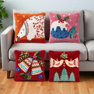 May include: Four square throw pillows with textured punch needle designs. Top left: orange with a white polar bear. Top right: pink with a Christmas pudding and bird. Bottom left: red with two bells. Bottom right: red with two birds and trees.