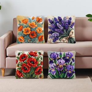 Peut inclure: Quatre coussins carrés avec des motifs floraux. L'un présente des coquelicots orange, un autre de la lavande, un troisième des coquelicots rouges et le dernier des iris violets. Les coussins sont sur un canapé rose et un tapis beige.