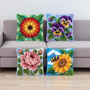 May include: Four decorative throw pillows with floral designs. The pillows feature a red and yellow flower, purple pansies, a pink rose, and a sunflower with a bee. The pillows are square and have a textured, handmade appearance.
