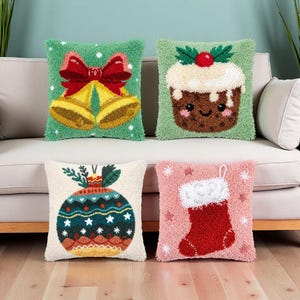 May include: Four square throw pillows featuring textured punch needle designs. One is green with yellow bells and a red bow, one is green with a Christmas pudding, one is cream with a colorful ornament, and one is pink with a red Christmas stocking.