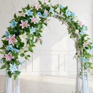 Peut inclure: Une arche de mariage en métal blanc ornée de lys roses, bleus et blancs et de feuillage vert. L'arche est en forme de demi-cercle et est placée contre un mur et un sol blancs. Les fleurs sont disposées en cascade sur l'arche.