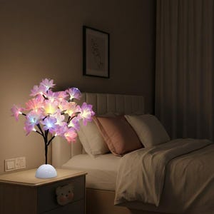 Può includere: Una lampada decorativa a forma di albero floreale con luci a LED multicolore. La lampada ha uno stelo nero e una base bianca, appoggiata su un comodino in legno. I fiori sono rosa, viola e bianchi, creando un bagliore soffuso nella camera da letto.