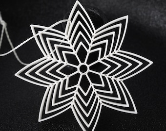May include: A white, geometric snowflake ornament with a layered design. The ornament has a star-like shape with pointed edges and a central circular opening. A white string is attached for hanging. The background is black.
