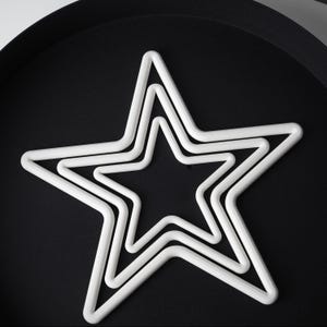 May include: Three white star-shaped decorations of varying sizes are nested together on a black surface. The stars are made of a thick, rounded material, creating a three-dimensional effect. The arrangement suggests a decorative or festive theme.