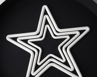 May include: Three white star-shaped decorations of varying sizes are nested together on a black surface. The stars are made of a thick, rounded material, creating a three-dimensional effect. The arrangement suggests a decorative or festive theme.